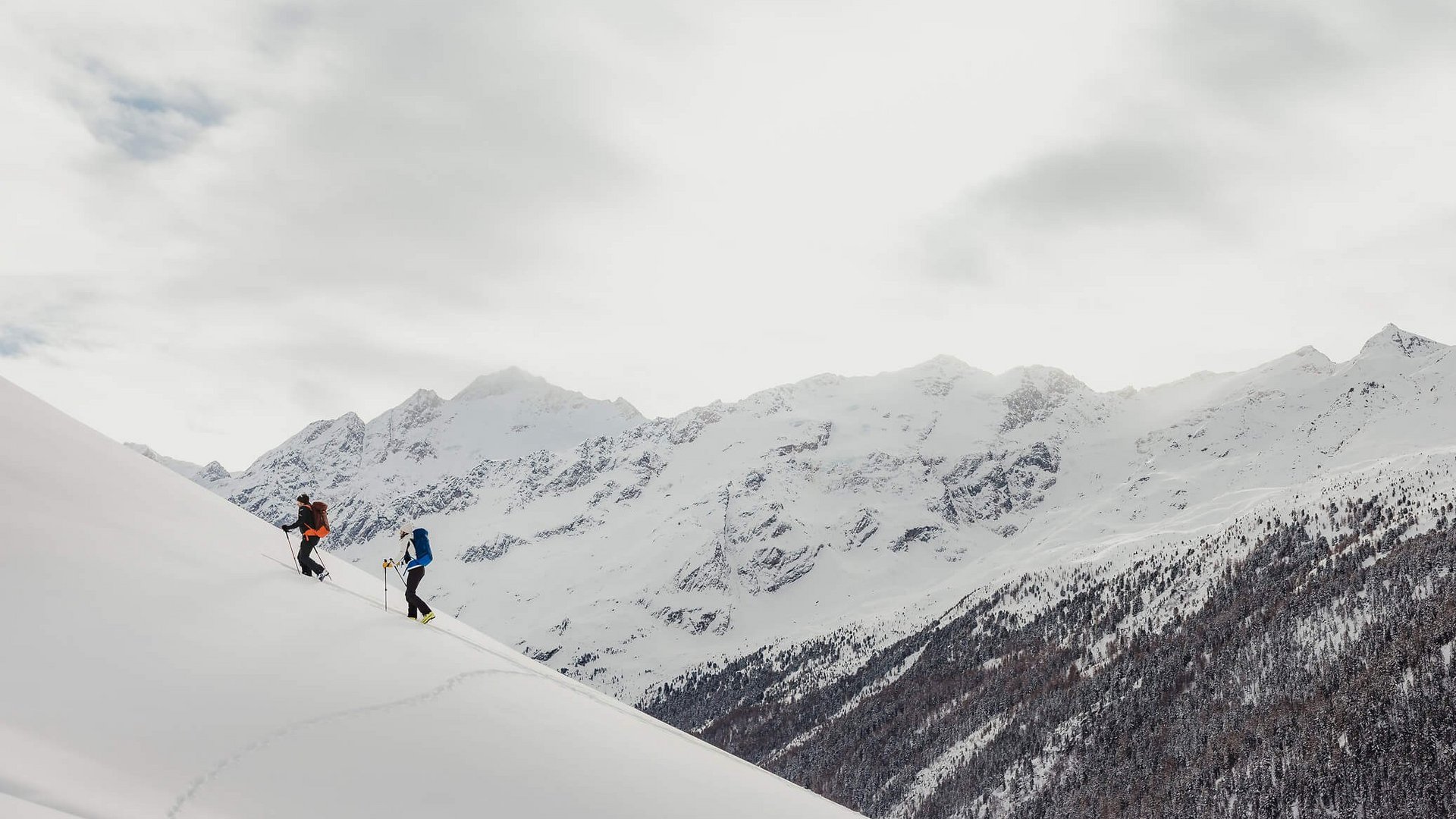 Zwei Skifahrer steigen einen schneebedeckten Hügel in den Bergen hinauf