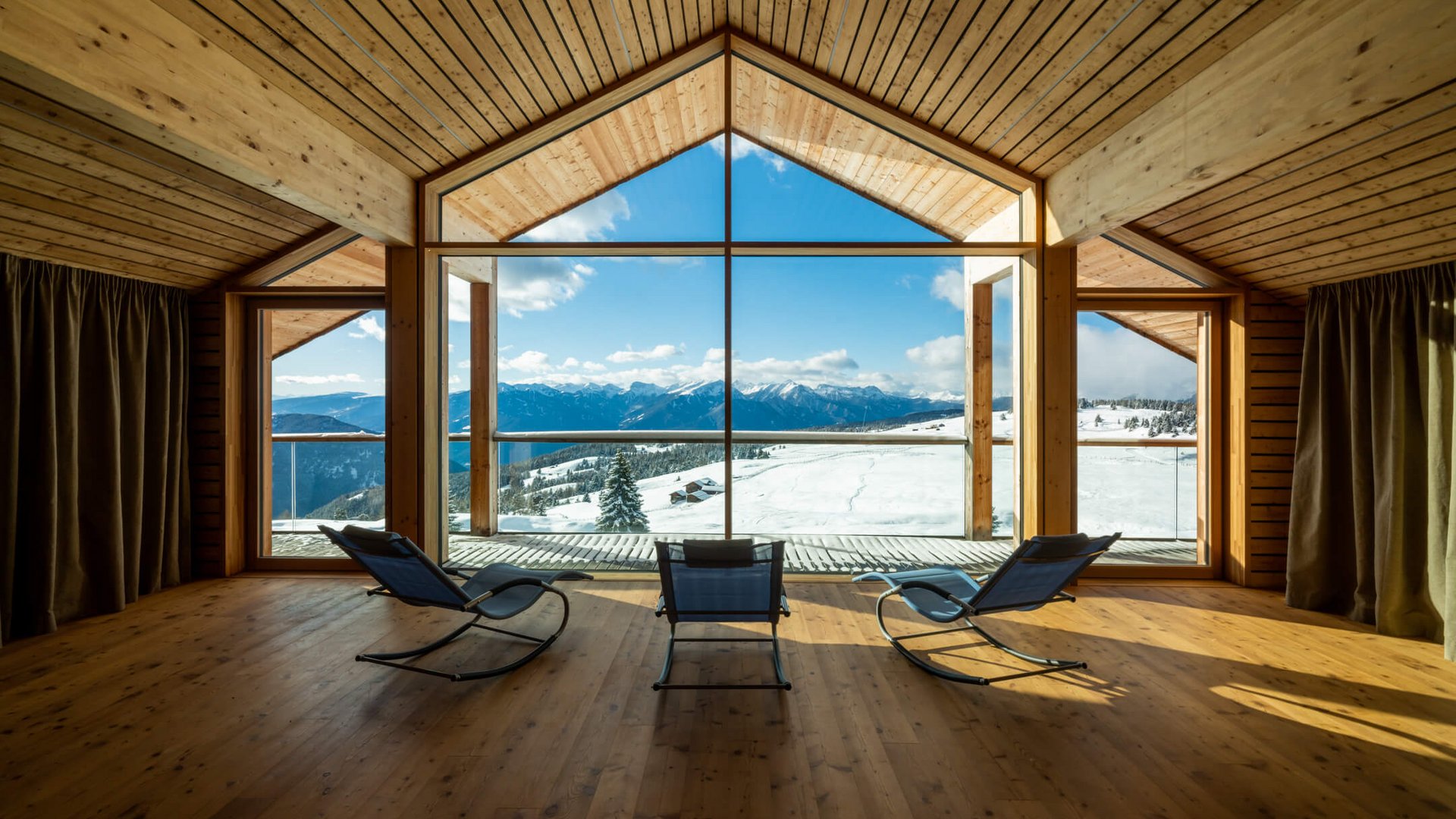 Moderne Holzhütte mit Panoramafenster und Blick auf verschneite Berge