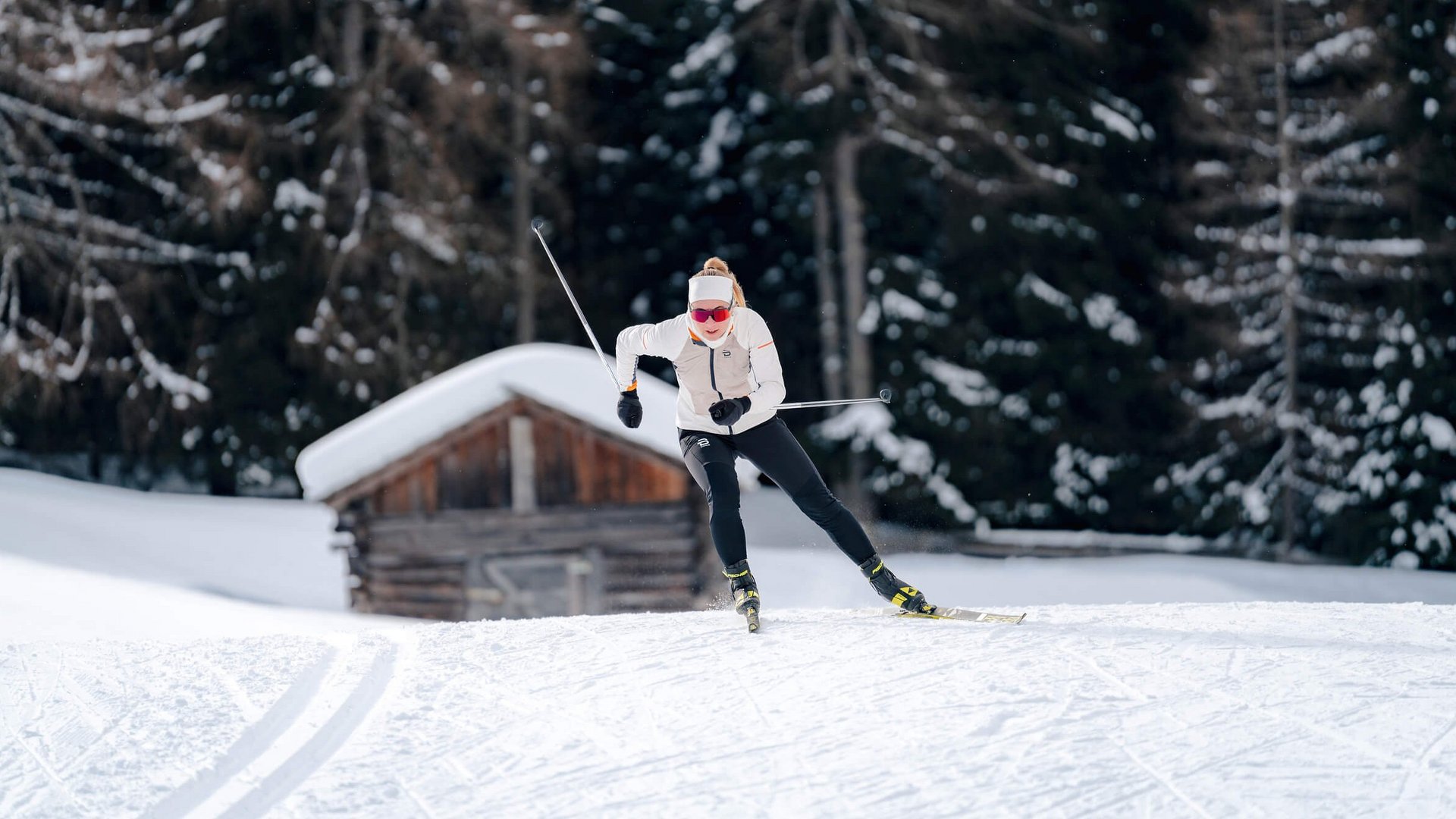 Frau beim Langlaufen vor verschneiter Hütte und Wald