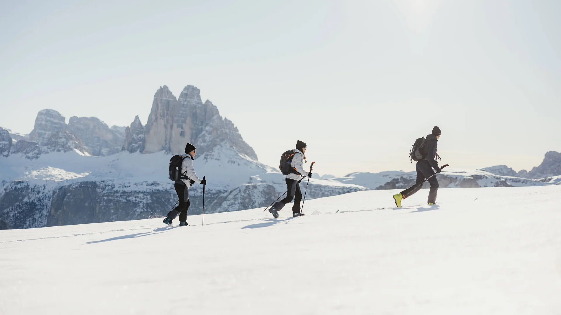 Drei Menschen beim Schneeschuhwandern vor Bergen im Schnee