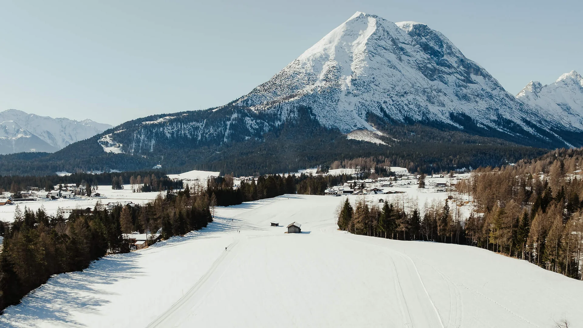 Schneesportler auf einer Loipe vor schneebedecktem Berg und Wald