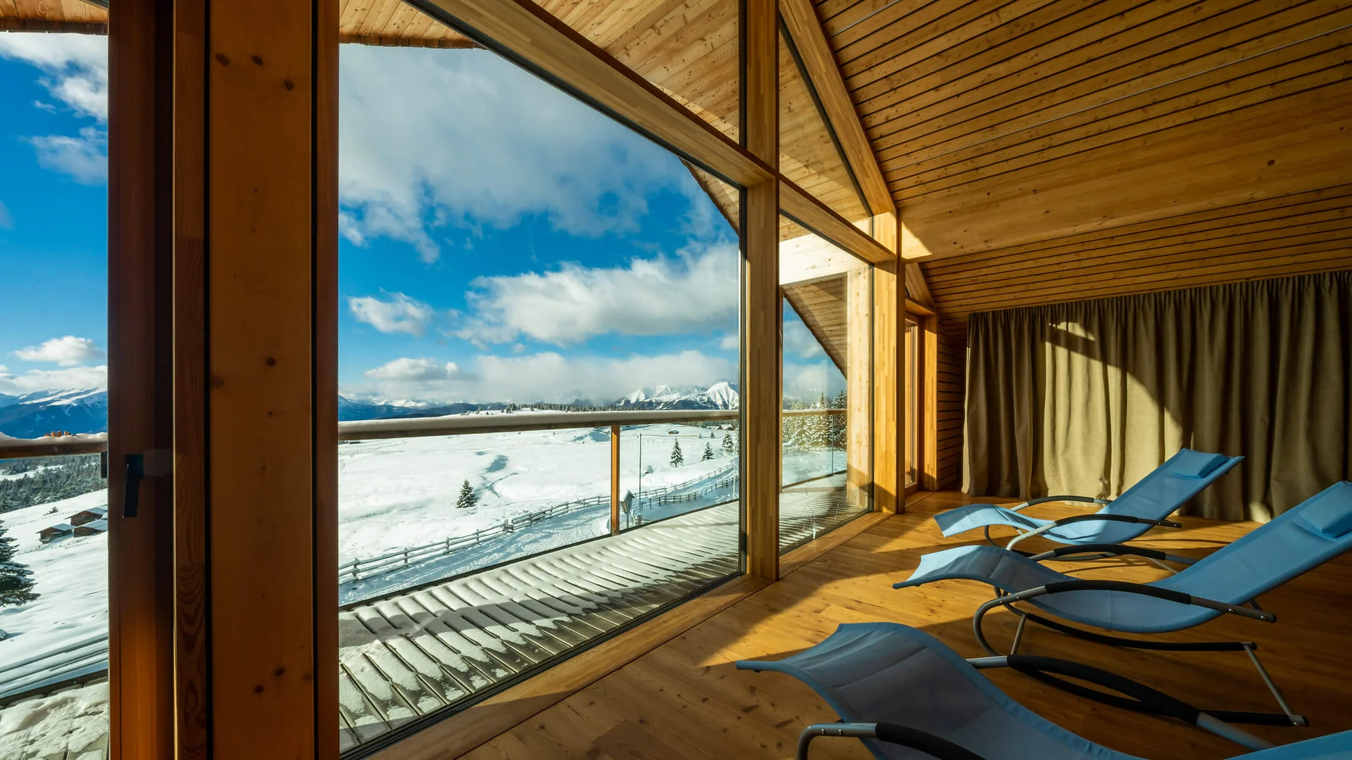 Alm-Hotel Starkenfeld Hütte ** © Jonas Eisenstecken Liegestühle in einem Holzraum mit Blick auf schneebedeckte Berge