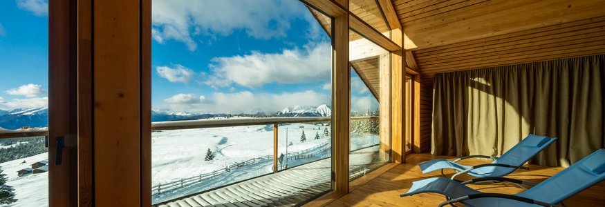 Liegestühle in einem Holzraum mit Blick auf schneebedeckte Berge