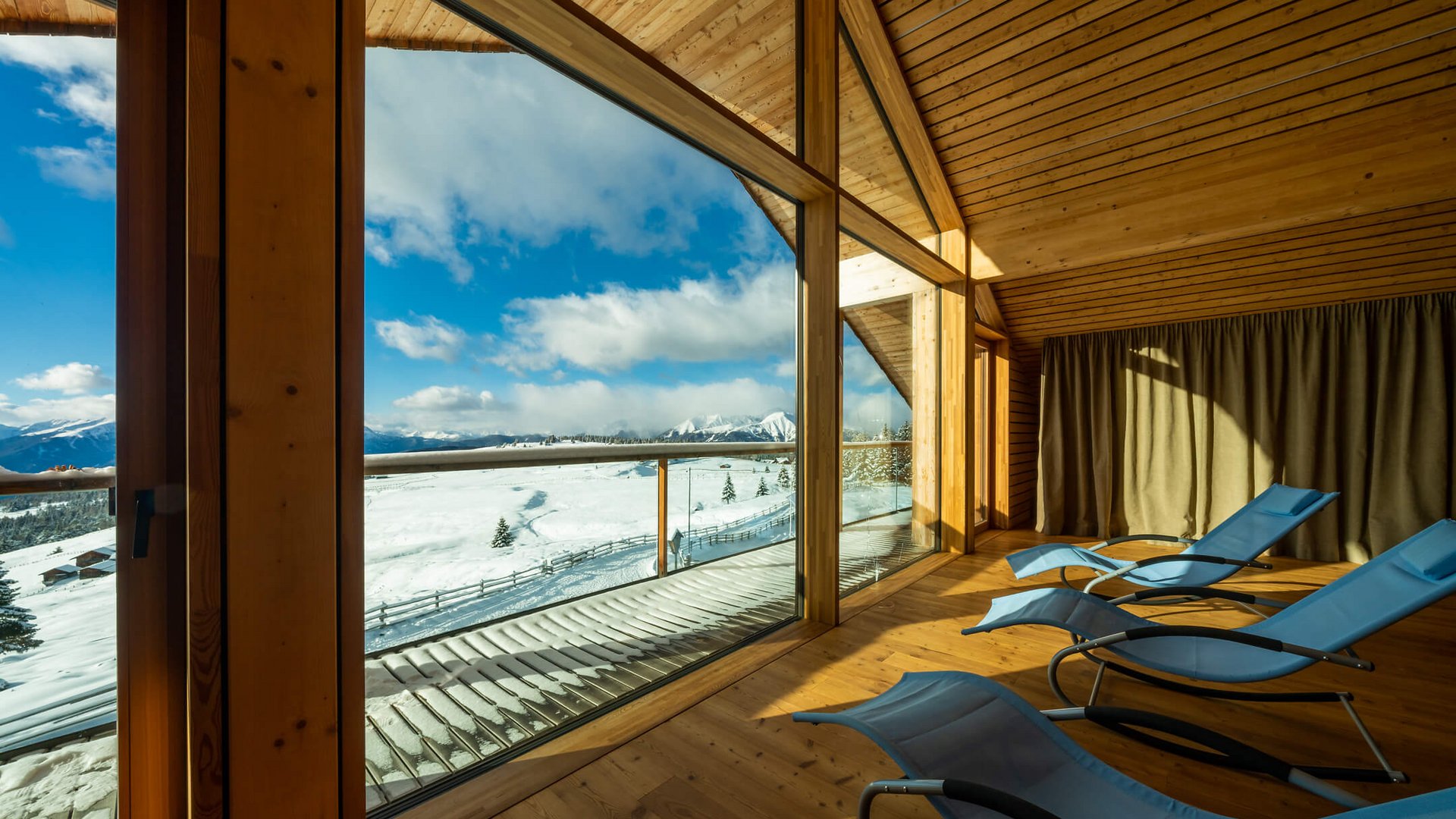 Liegestühle in einem Holzraum mit Blick auf schneebedeckte Berge