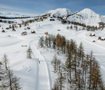 Snow-covered Alps with chalets and cross-country skiers under clear sky
