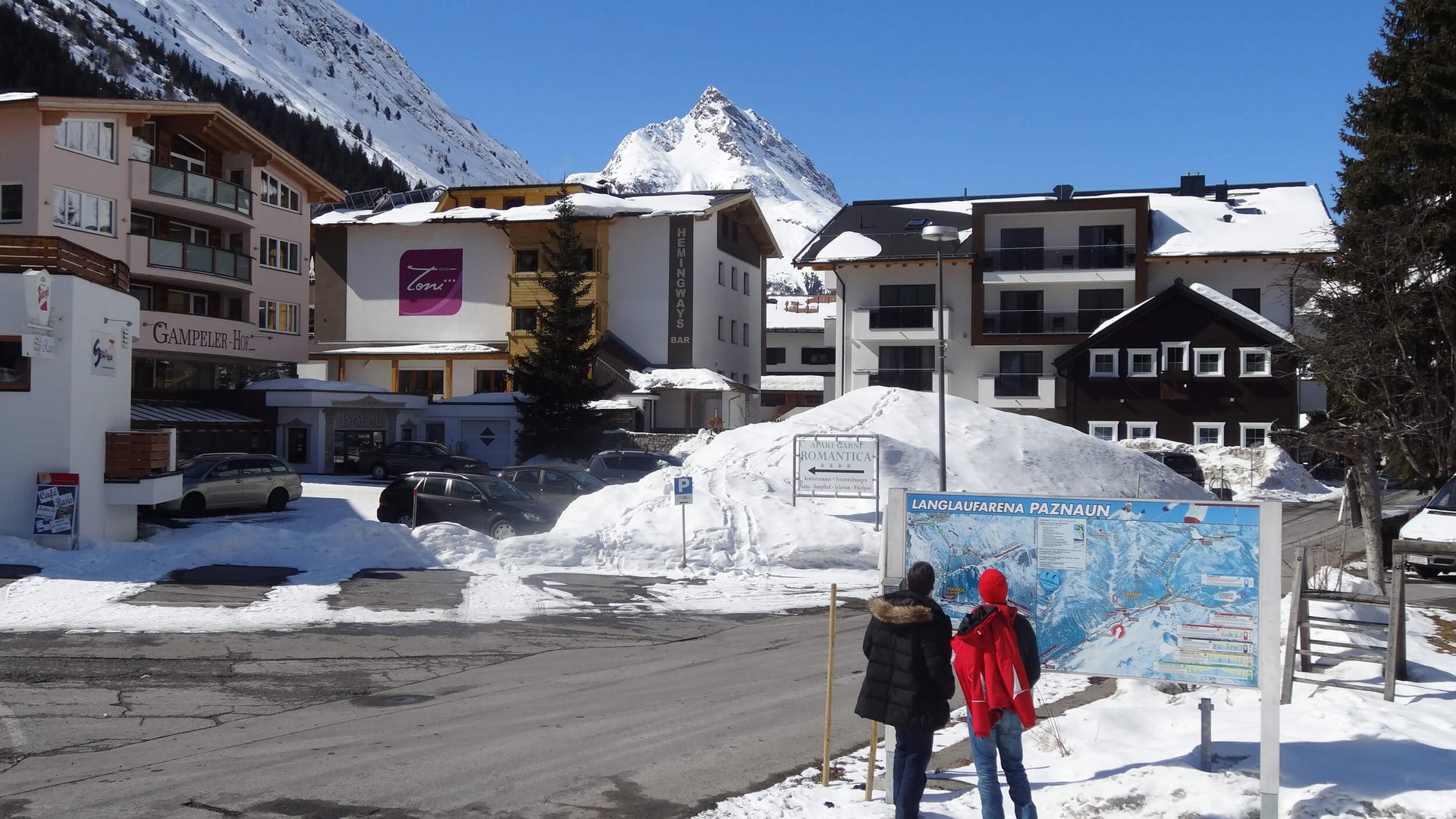 Two people reading a map in snowy village with mountains in background