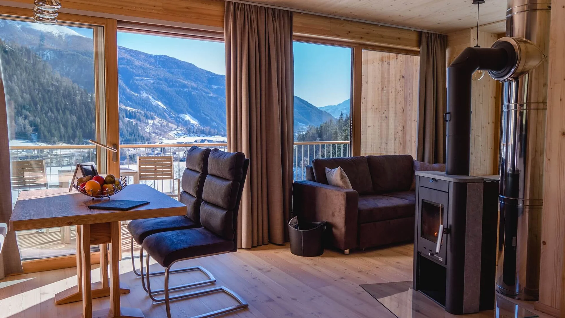 Wohnzimmer mit Kamin, Sofa, Esstisch und Bergblick durch große Fenster