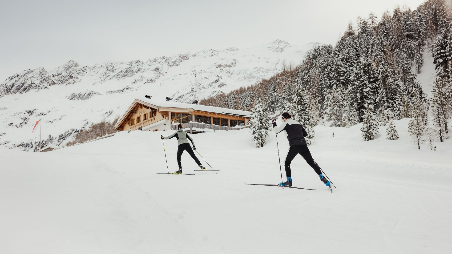 Zwei Langläufer vor verschneiter Berghütte im Winter