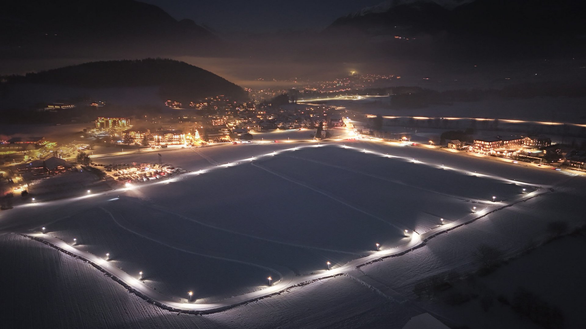 Befestigte Straßen und beleuchtete Gebäude in verschneiter Landschaft bei Nacht