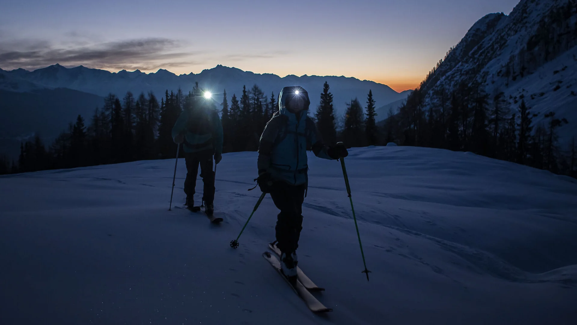 Skitouren Urlaub in Ratschings © Ratschings Tourismus - Manuel Kottersteger Zwei Skifahrer mit Stirnlampen bei Dämmerung in verschneiter Berglandschaft