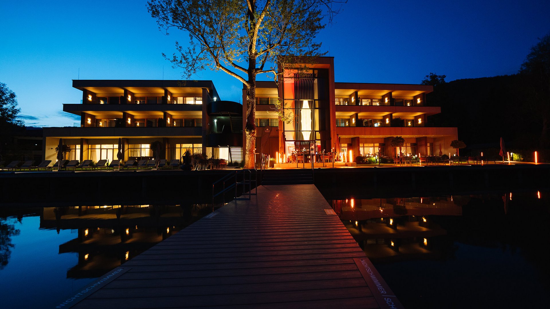 Illuminated modern hotel at night with water reflection and dock