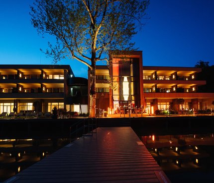 Beleuchtetes modernes Hotel bei Nacht mit Wasserspiegelung und Steg