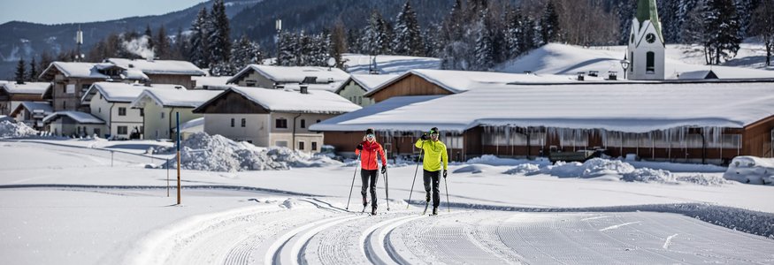 Two cross-country skiers on groomed trail near snowy village and mountains