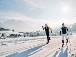 Kleinwalsertal © Kleinwalsertal Tourismus - Oliver Farys Zwei Langläufer auf einer verschneiten Loipe vor einem Bergdorf