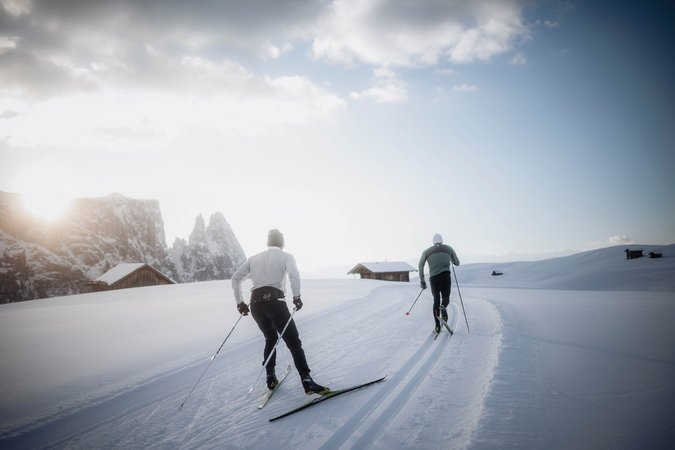 Langlauf Urlaub © Seiser Alm Marketing - Manuel Kottersteger Zwei Langläufer fahren auf einer verschneiten Landschaft bei Sonnenaufgang