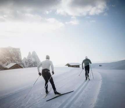 Zwei Langläufer fahren auf einer verschneiten Landschaft bei Sonnenaufgang
