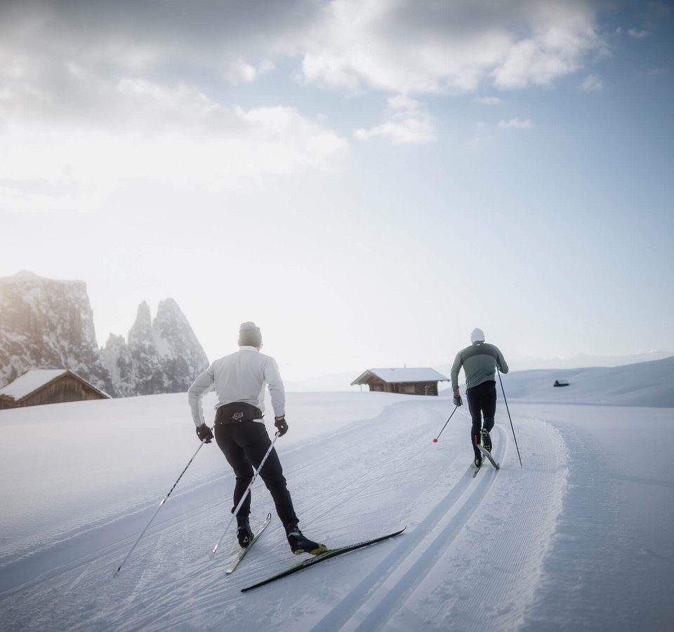 Best of Dolomitenregion Seiser Alm © Seiser Alm Marketing - Manuel Kottersteger Zwei Langläufer fahren auf einer verschneiten Landschaft bei Sonnenaufgang
