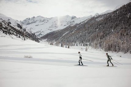 Zwei Personen Langlauf in verschneiter Berglandschaft mit Nadelwald