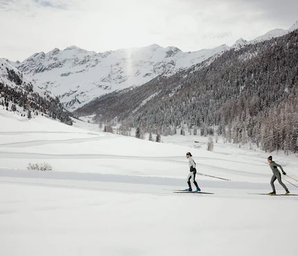 Zwei Personen Langlauf in verschneiter Berglandschaft mit Nadelwald