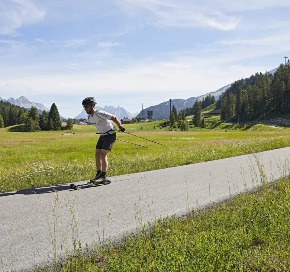 Mann beim Rollerski in einer grünen Berglandschaft auf einem Asphaltweg