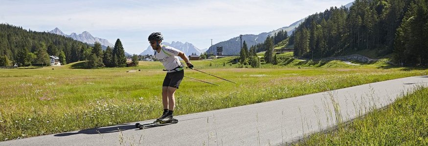 Mann beim Rollerski in einer grünen Berglandschaft auf einem Asphaltweg