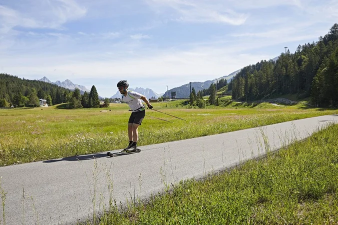 Mann beim Rollerski in einer grünen Berglandschaft auf einem Asphaltweg