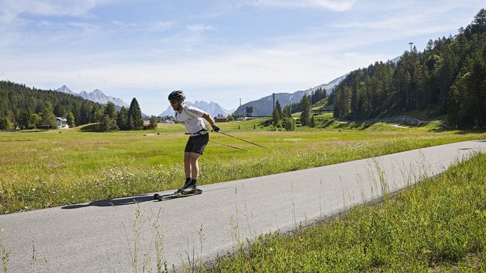 Mann beim Rollerski in einer grünen Berglandschaft auf einem Asphaltweg