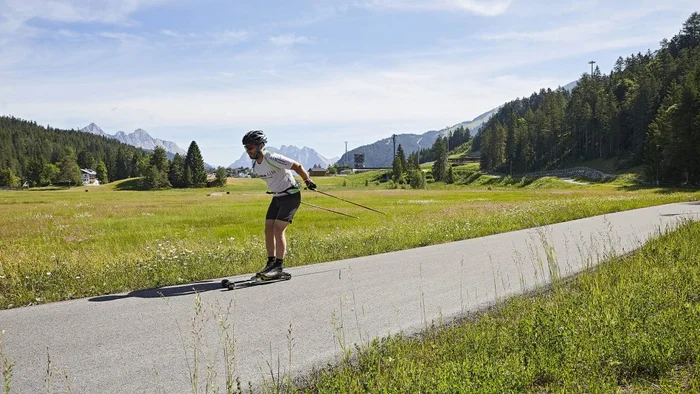 Mann beim Rollerski in einer grünen Berglandschaft auf einem Asphaltweg