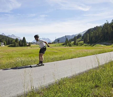 Mann beim Rollerski in einer grünen Berglandschaft auf einem Asphaltweg