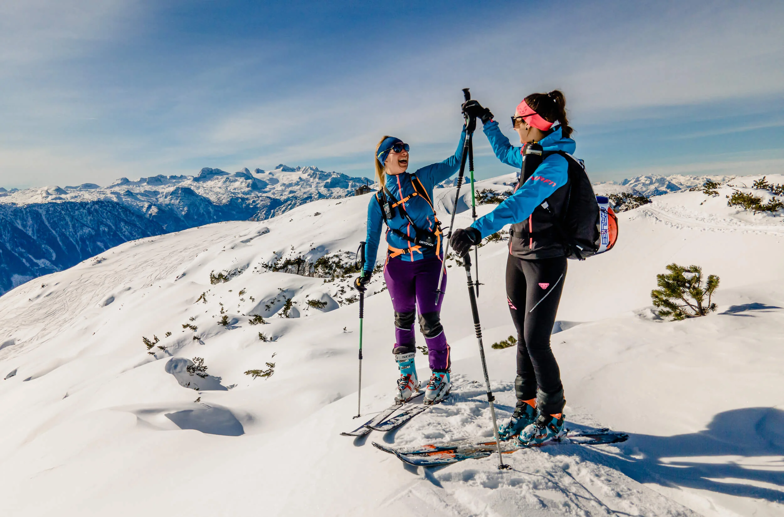 Two women ski touring on a snowy mountain high-fiving