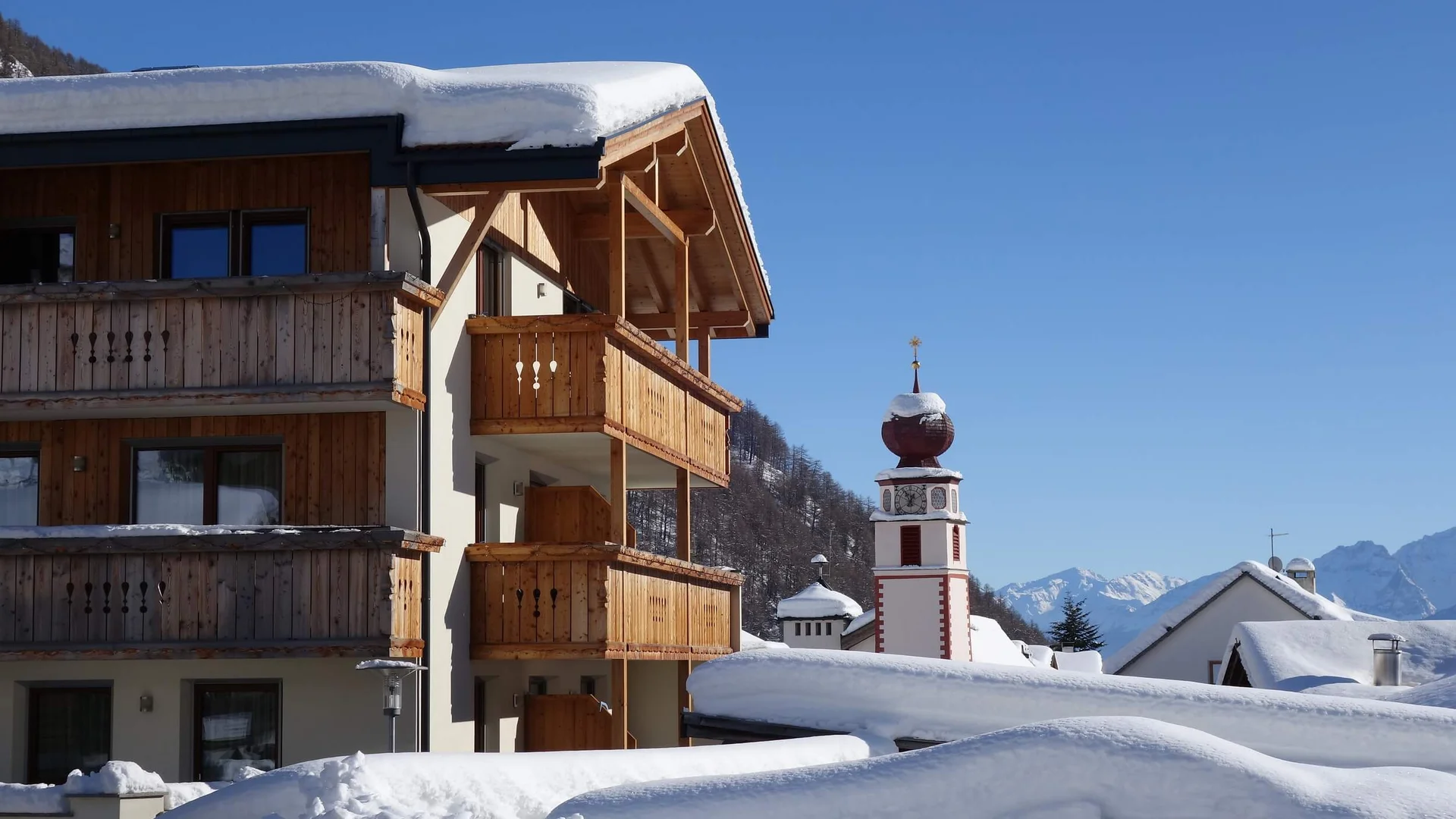 Snow-covered wooden chalet and clock tower in an Alpine village