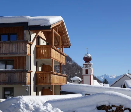 Schneebedecktes Holzalmenhaus und Uhrturm in einem Alpenort