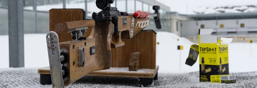 Präzisionsgewehr auf Schneetisch mit Munition und Zielscheiben im Hintergrund