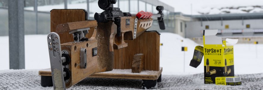 Präzisionsgewehr auf Schneetisch mit Munition und Zielscheiben im Hintergrund