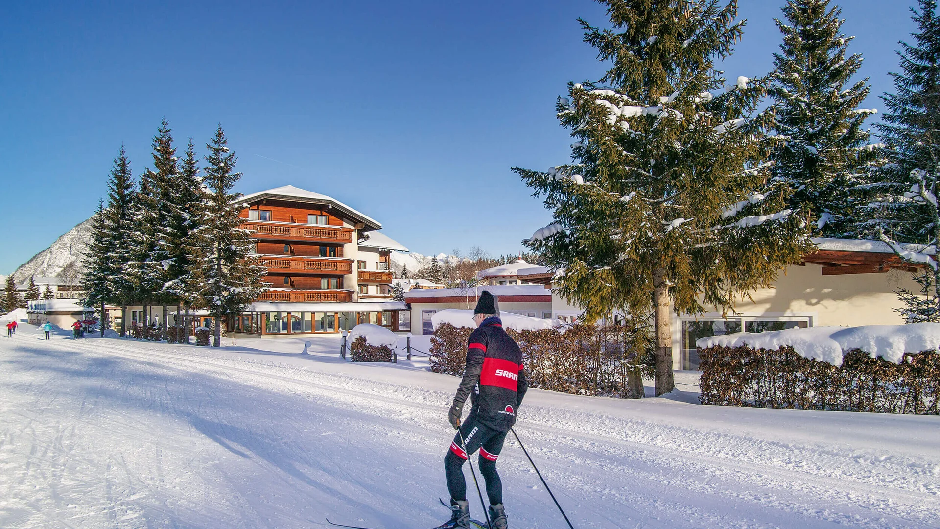 Alpenhotel Karwendel **** © Hotel Karwendel Bernhard Rödlach BetriebsGmbH Langläufer vor verschneitem Hotel und Tannenbäumen bei klarem Himmel