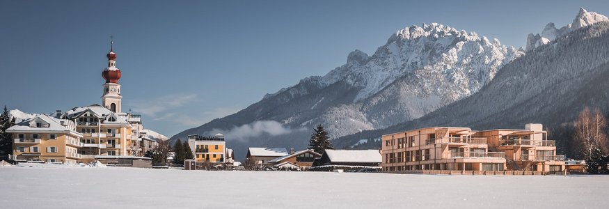 Snow-covered village with church and modern buildings near Alpine mountains