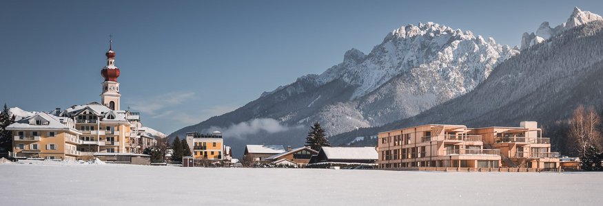 Schneebedecktes Dorf vor den Alpen mit Kirche und modernen Gebäuden