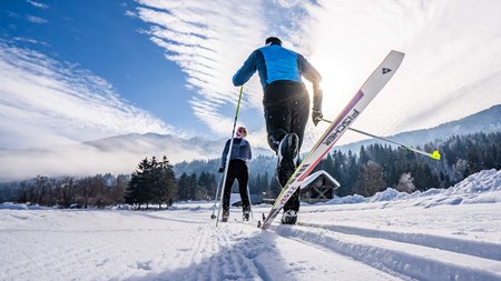 Zwei Langläufer fahren auf schneebedeckter Spur in winterlicher Landschaft