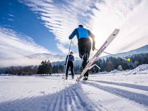 Zwei Langläufer fahren auf schneebedeckter Spur in winterlicher Landschaft