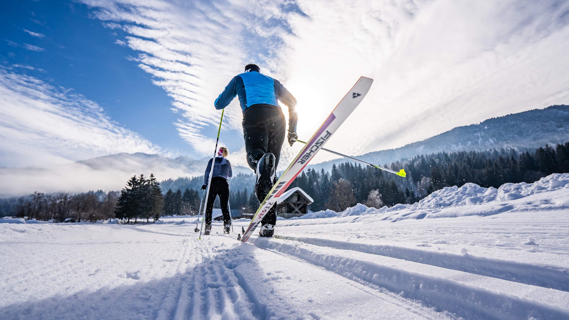Zwei Langläufer fahren auf schneebedeckter Spur in winterlicher Landschaft