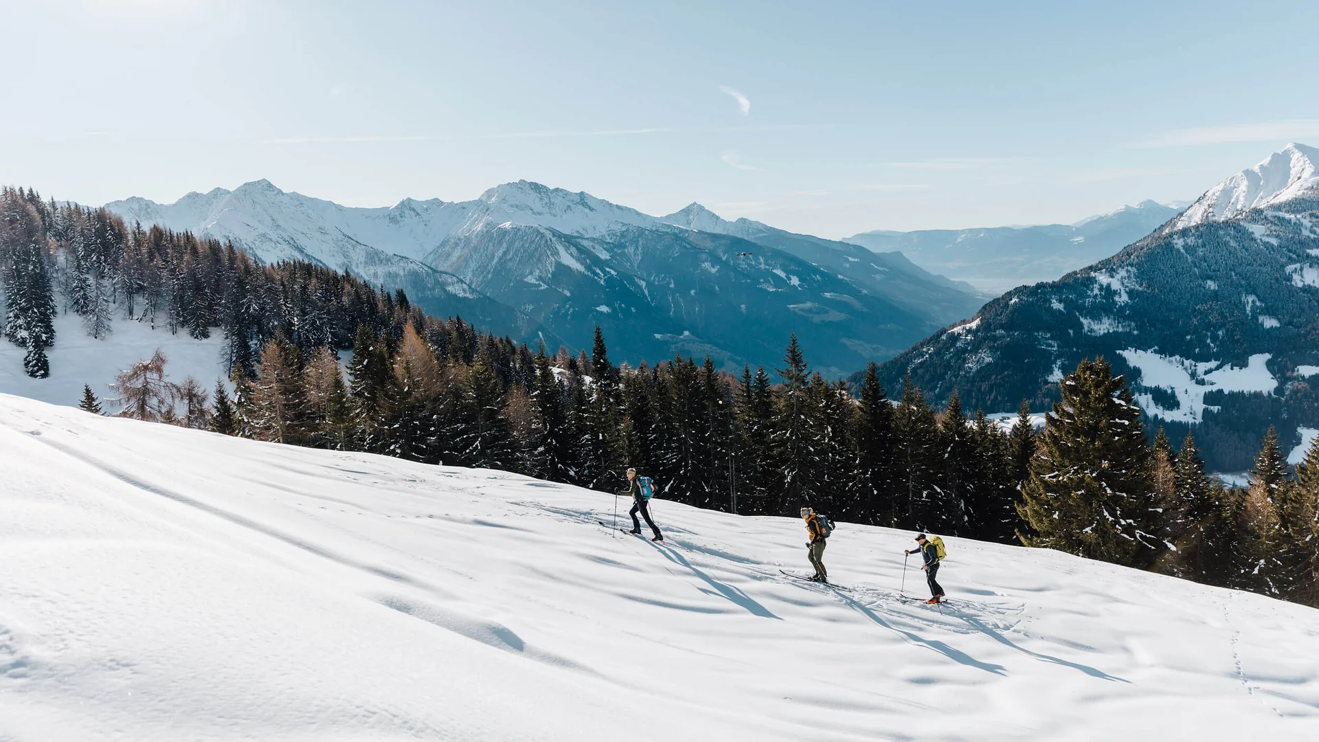 Drei Skitourengeher in verschneiter Berglandschaft bei klarem Himmel