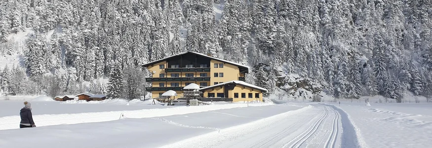 Schneebedecktes Haus am Fuß eines verschneiten Waldberges bei blauem Himmel