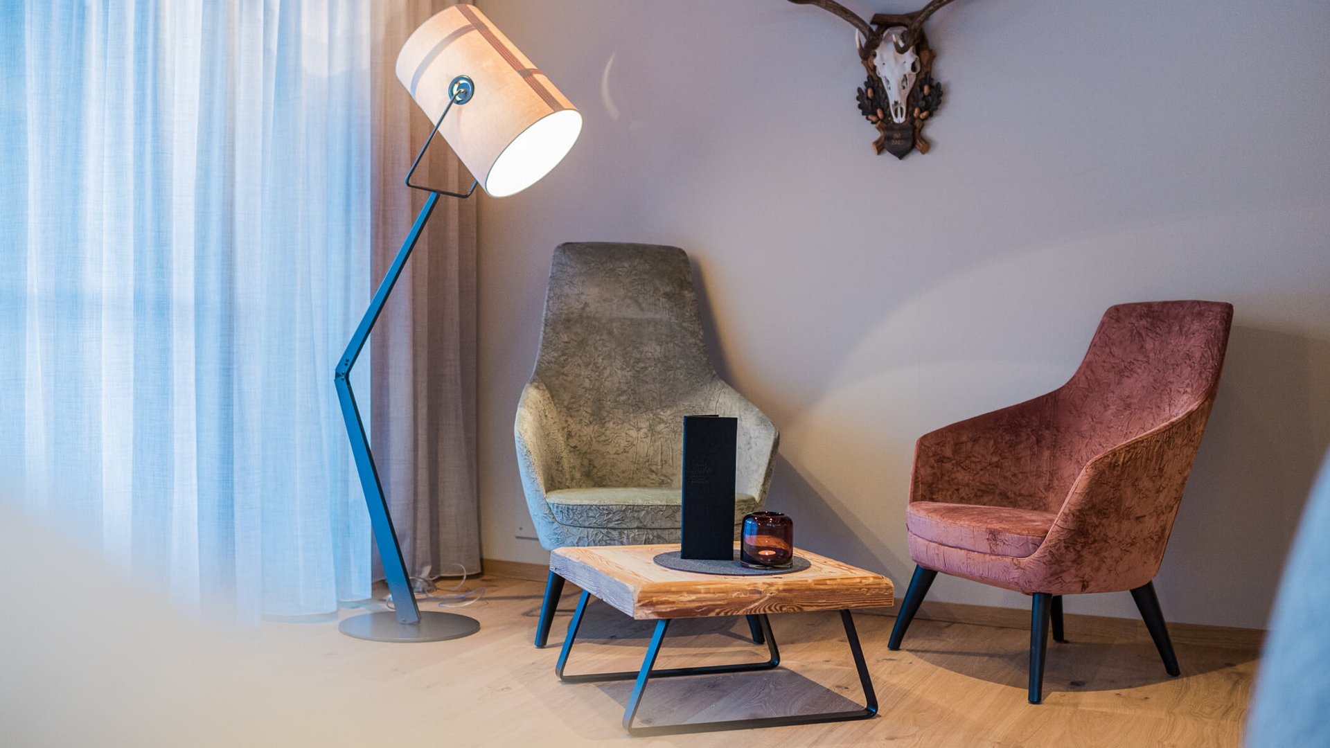 Wohnzimmer mit zwei Sesseln, Holztisch, Stehlampe und Hirschgeweih an der Wand