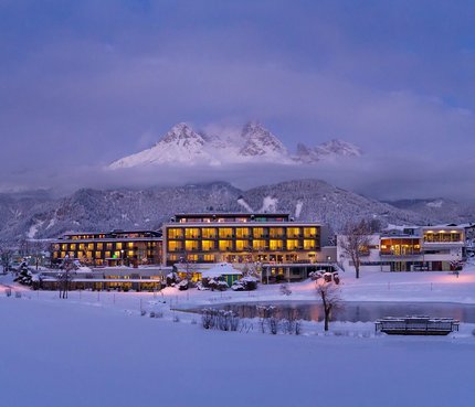 Ritzenhof - Hotel und Spa am See © Stefan Gimpl Beleuchtetes Hotel im verschneiten Tal vor bewölktem Berggipfel bei Abenddämmerung