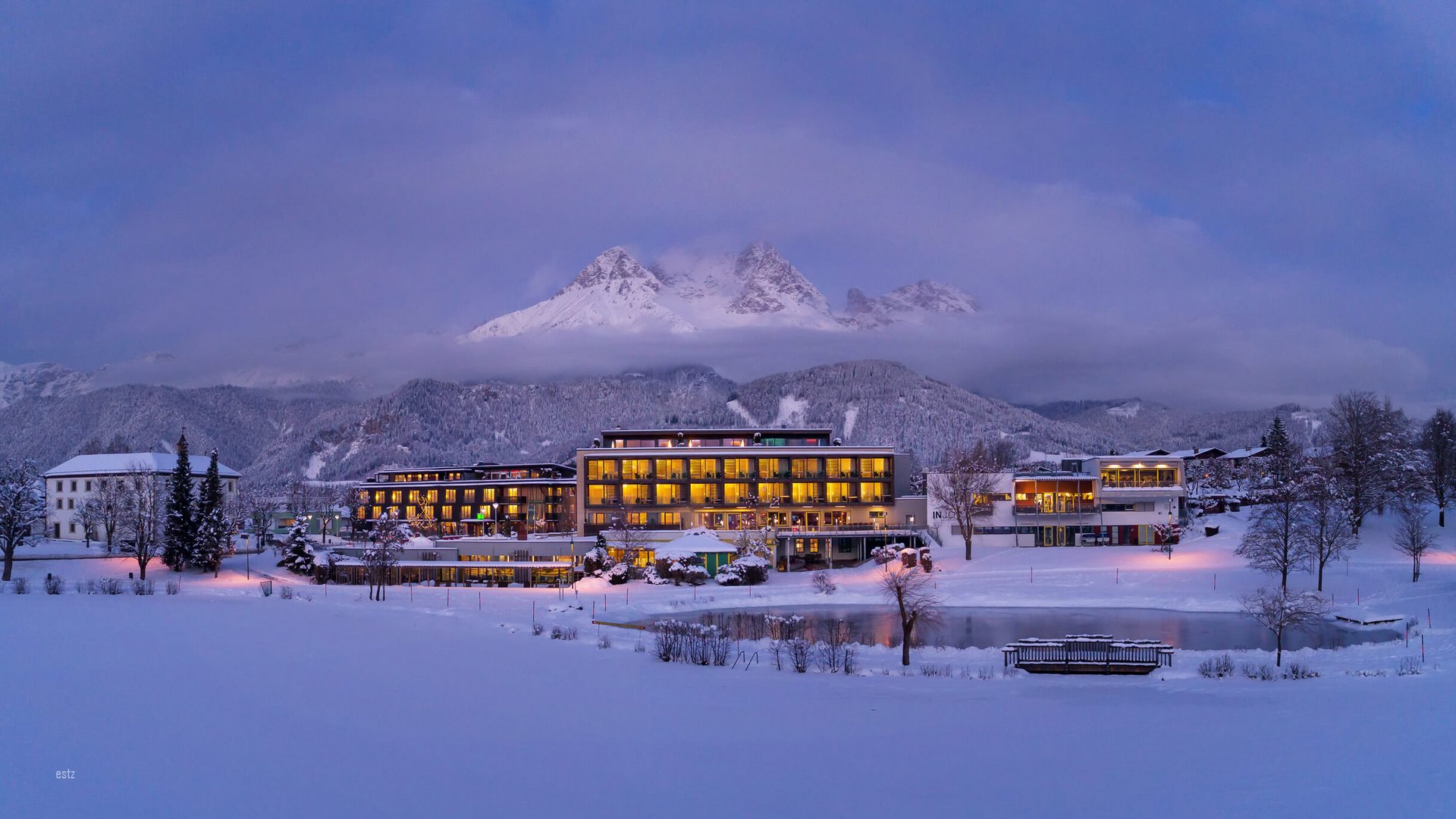 Lit hotel in snowy valley with cloudy mountain peak at dusk