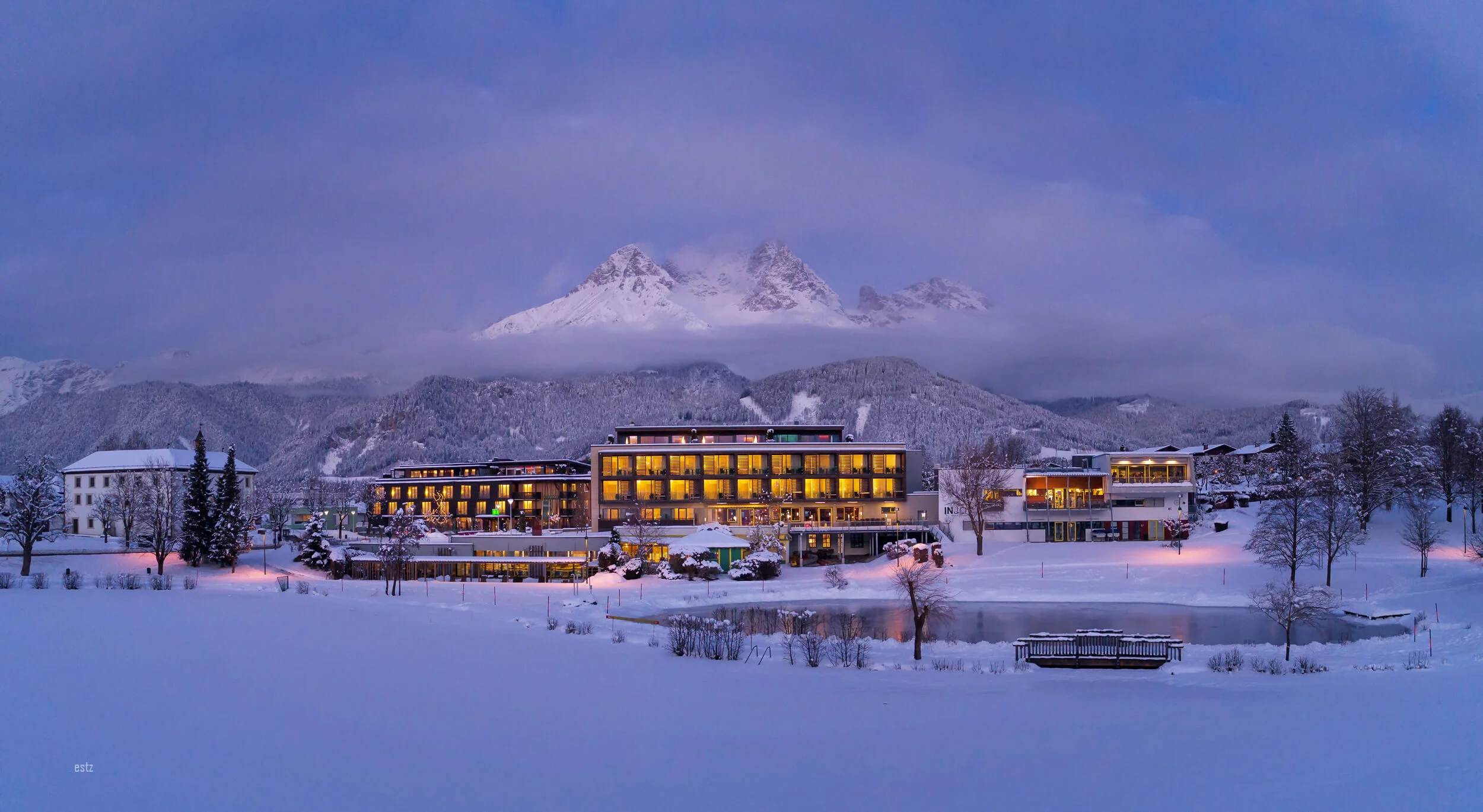 Lit hotel in snowy valley with cloudy mountain peak at dusk