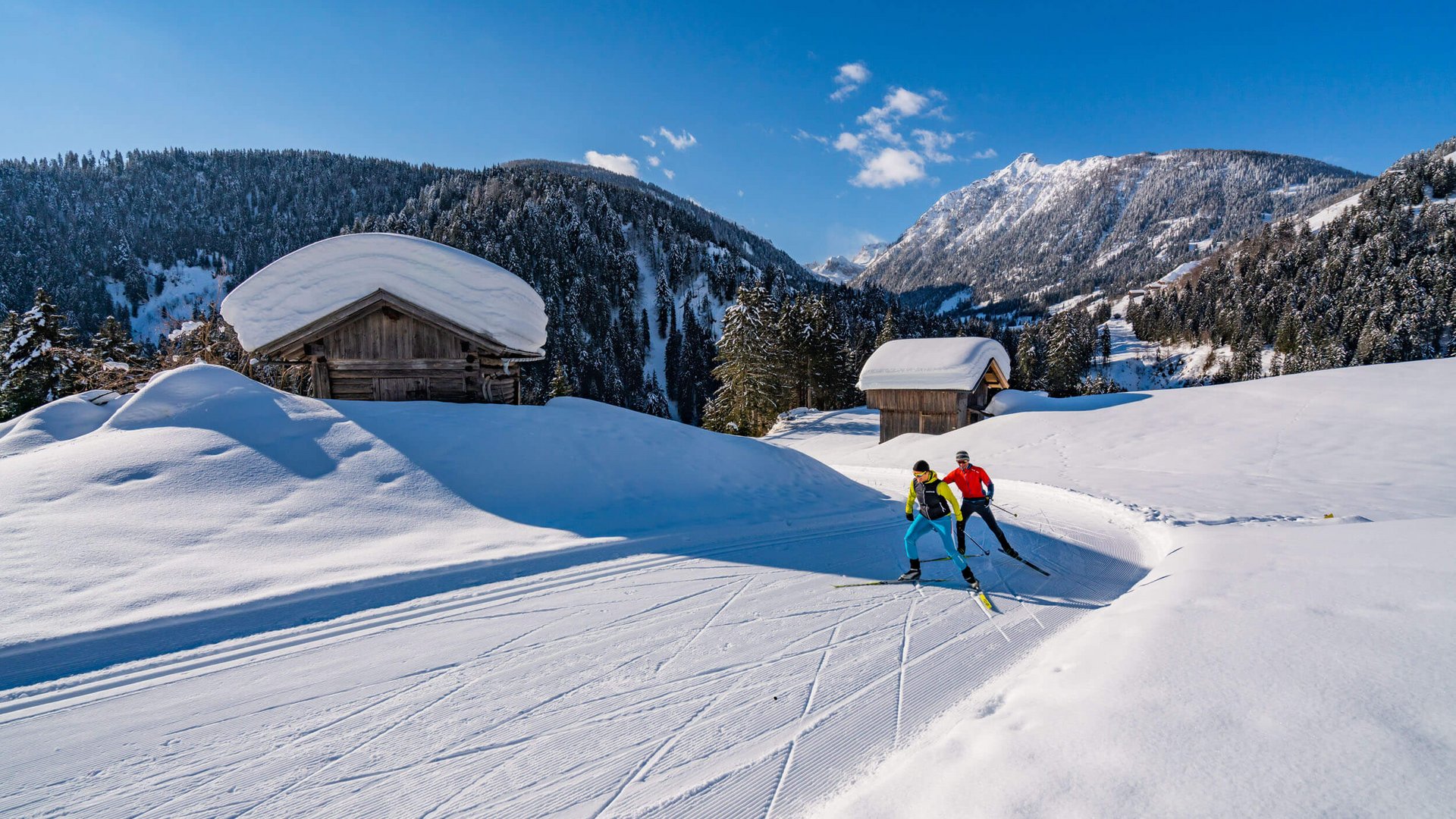Zwei Langläufer auf schneebedeckter Loipe in winterlicher Berglandschaft