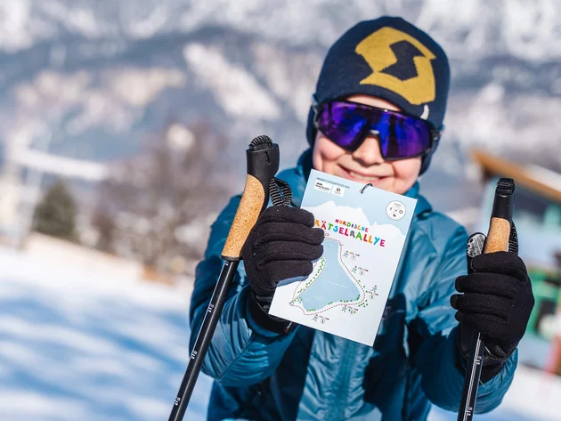 Kind mit Wintersportausrüstung hält eine Karte für eine nordische Rätselrallye