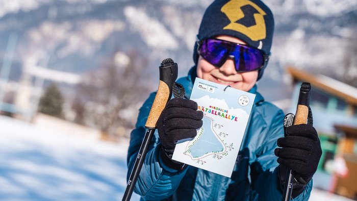 Kind mit Wintersportausrüstung hält eine Karte für eine nordische Rätselrallye