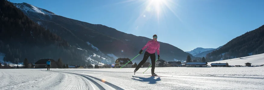 Cross-country skier on snowy trail under bright sun in mountain valley